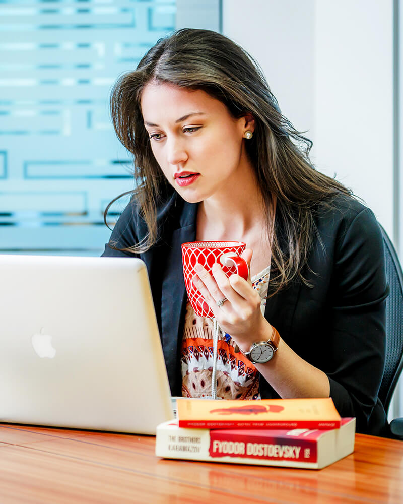 Woman at desk with laptop holding a hot drink in a mug