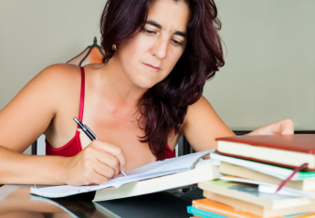 Spanish woman taking notes with pen in front of a large pile of books
