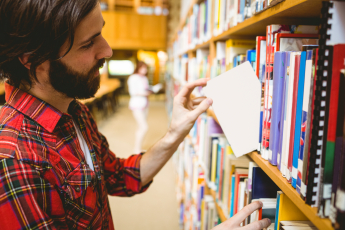 man with beard in library choosing a small book from a shelf