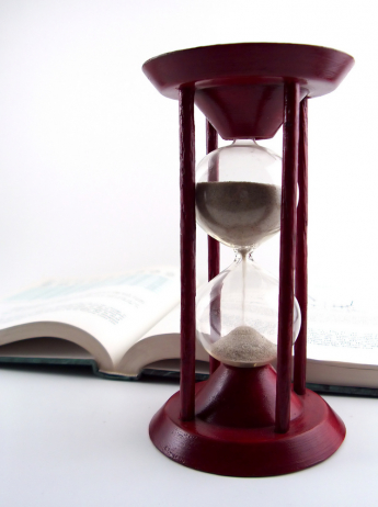 an old fashioned hourglass running out in front of an open book