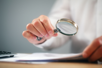 A person using a magnifying glass, reading through a document to find errors