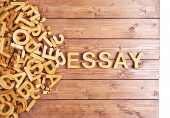 Word 'essay' made with block wooden letters next to a pile of other letters over a wooden board surface composition