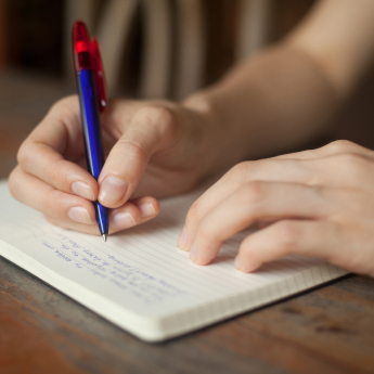 A person writing on a notebook with a blue pen with red cap