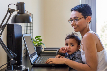 Mom holding her baby boy while working on a laptop