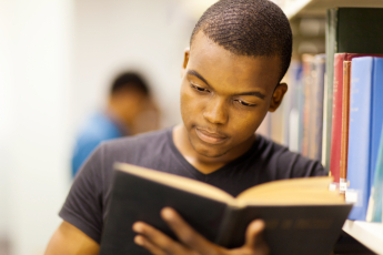 Male student reading a book in a library, feeling relaxed