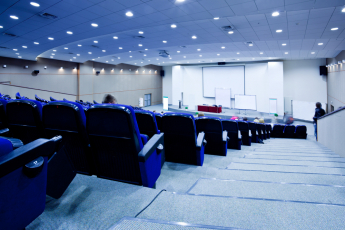 A lecture theatre with blue seats and some students sitting