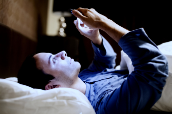 A man lying in bed watching something on a smartphone