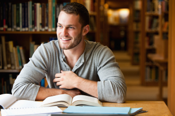 Male student reading a book in a library, smiling