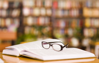 Eye-glasses on a book with bookshelves in the background