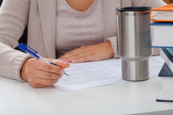 A woman writing on a paper, with stainless steel mug in front of her